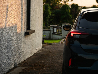 Wall Mural - A black car is parked in front of a white building. The car is dark and has a red light glowing on the back. The sunset scene is quiet and peaceful. Coming back home late after work theme
