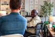 © Jovo Jovanovic/Stocksy - Man in wheelchair conversing with another person indoors.