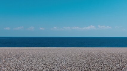 Poster - Endless expanse of deep blue sea meeting a vast pebble beach under a serene sky dotted with small white clouds, creating a tranquil and minimalist seascape