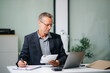 © laddawan - Confident businessman working on finance analysis with a tablet and laptop at office desk. Perfect for business