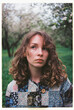 © Viktor Solomin/Stocksy - Young woman in a patchwork shirt stands among blooming trees