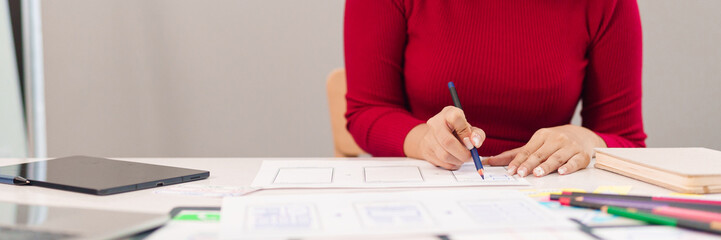 Canvas Print - asian woman user interface designer sketches mobile app layouts with pencil on paper in creative des