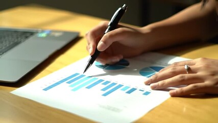 Poster - Analyzing Financial Graph with Black Pen on Paper Next to Laptop on Wooden Desk in Bright Light