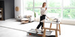 © Pixel-Shot - Young businesswoman with coffee cup training on treadmill at table in office