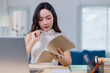 © Tj - Young woman deeply engaged in reading and analyzing documents at her desk, surrounded by office supplies, in a bright and modern workspace with a laptop nearby