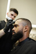 © Dmytro Hai - Blurred barber trimming head of bearded african american customer