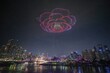 © UQink - Colorful drone show of rose shape over night skyline with illuminated cityscape and river