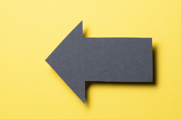 Poster - Black cut out blank paper cardboard arrow direction sign with copy space for text on yellow background, flat lay top view pointing symbol conceptual message backdrop