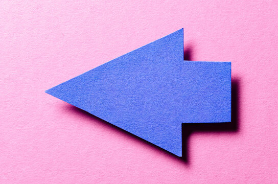Blue cut out blank paper cardboard arrow direction sign with copy space for text on pink background, flat lay top view pointing symbol conceptual message backdrop