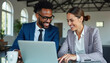 © jack - Two African-American business professionals in an office, with a man smiling while using a laptop and a woman observing beside him with a coffee cup, showing a pleasant collaborative atmosphere.