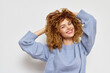 © SHOTPRIME STUDIO - Smiling woman with curly hair wearing a light blue sweater, posing playfully against a neutral background, radiating joy and confidence in a modern lifestyle context