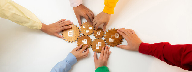 Poster - A diverse group of hands work together on wooden gears, symbolizing teamwork and collaboration during a strategic management session focused on innovative solutions. Amity