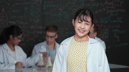 Poster - Cute asian scientist smile to camera while diverse group doing experiment. Young happy schoolgirl standing at blackboard with chemical theory written while wearing lab coat at laboratory. Edification