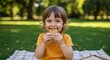 © NN AI - Happy child eating granola bar in yellow shirt during outdoor picnic. Toddler with curly hair enjoying healthy snack on checkered blanket in park. Nutrition and recreation concept