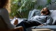 © Justlight - An office setting features a man lying back on a sofa visibly relieved as he expresses his thoughts while a therapist listens intently holding a notepad for observations. The surrounding
