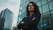 © hatam - Confident woman in a black business suit with arms crossed looking up in front of office buildings