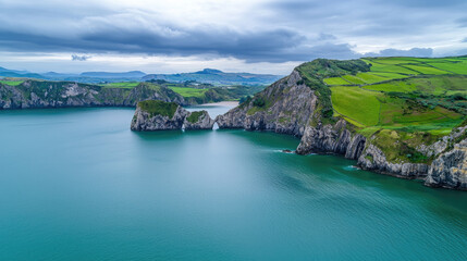 Poster - Dramatic cliffs tower over tranquil green ocean cove, lush fields and rolling hills under cloudy sky create peaceful landscape