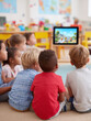 © SolaruS - Diverse young children captivated, watching a screen together in a bright classroom. Depicts learning, togetherness, education, and technology in early childhood.