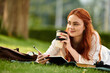 © Bliss - Young woman enjoys her leisure time with a coffee and notebook in a sunny park setting