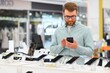 © Serhii - guy in an electronics store chooses a cell phone to buy