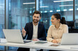 © Liubomir - A man and woman in a business meeting at a desk, discussing ideas while looking at a laptop.