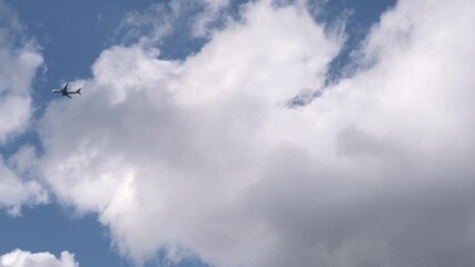 Aufkleber - A plane glides smoothly through a clear sky filled with fluffy clouds, showcasing a serene afternoon atmosphere with bright sunlight illuminating the scene.