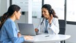 © NafiliaEmil - A Hispanic Latin female doctor conducts an online video call to consult with a patient on a laptop. A young medical assistant, also a woman, serves as a therapist via videoconferencing to a web camera