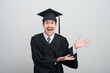 © PhugunStock - A young man in a graduation gown and cap smiles at the camera, striking a confident pose to celebrate his academic achievement on graduation day.