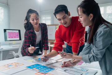 Fototapete - Three asian ux designers working together on developing an app interface wireframe for a mobile application, analyzing user experience and user interface together in the office