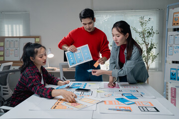  - Creative team actively engaged in designing a mobile app interface, using printed wireframes and digital tools in a modern office setting. Collaboration and innovation are emphasized