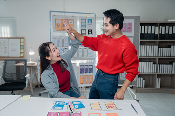 Fototapete - Two enthusiastic UI/UX designers sharing a high-five, celebrating their successful collaboration on a mobile app interface design in a vibrant, modern office environment