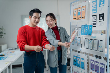 Fototapete - Two young Asian ui/ux web designers comparing printed mobile app templates at the office, working together on user interface and user experience functionality and usability
