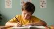 © Bakha - Focused young boy in yellow shirt sitting at desk doing homework with colored pencils, studying attentively in well lit classroom with pastel walls