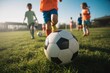 © antusher - Kids play soccer on the grass field with a white and black soccer ball in the foreground outdoors