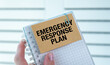 © Pawel - A person is holding a notebook with the words Emergency Response Plan written on it. The notebook is open to a page with a clip holding the paper in place