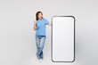 © ViDi Studio - Full body young woman wear blue t-shirt casual clothes big huge blank screen mobile cell phone smartphone with area do winner gesture isolated on plain solid white color background. Lifestyle concept