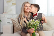 © New Africa - Little boy kissing his smiling mother with bouquet of beautiful chamomile flowers on sofa at home