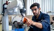 © photostockatinat - A focused engineer inspecting a robotic arm in a modern factory. He wears glasses and a blue uniform, pointing at the machinery with precision