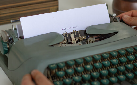 Close-up of a vintage typewriter with the phrase make it happen typed on a sheet of paper, suggesting a writer or journalist working on a motivational or inspirational piece