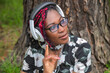 © Jacques Durocher - Happy African American Woman with Colorful Braids Listening to Music with Headphones in Park