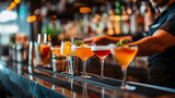 Vibrant cocktails line up at a dimly lit bar, ready to be served for a night party. A row of modern cocktails on a bar is the focal point, complemented by a blurred background of bottles and bartender
