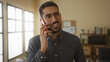 © Krakenimages.com - Man talking on smartphone in modern office with glasses smiling confidently in casual shirt near desk during a phone call in bright indoor setting showing business atmosphere.