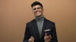 © Krakenimages.com - Young man smiling and clapping with confidence against an isolated brown background, highlighting his stylish attire and positive demeanor.
