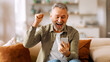 © Home-stock - Surprised excited senior man holding smartphone, reading good news and clenching fist, amazed by online win, being overjoyed by victory success