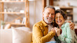 © Home-stock - Happy elderly partners. Senior man and woman sharing tender moment, hugging and radiating happiness, sitting on sofa in living room and smiling at camera