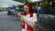 © Krakenimages.com - Woman examining her wrist on a bustling city street, wearing a red scarf and white shirt, surrounded by blurred outdoor cafes and pedestrians in the background.