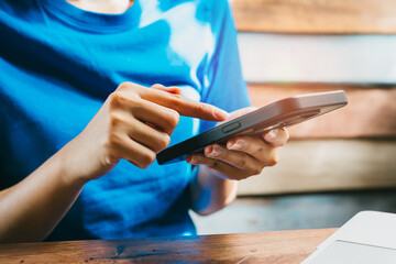 Poster - Woman using smartphone. Person in Blue Shirt Interacting with Smartphone at Wooden Table Surrounded by Natural Light