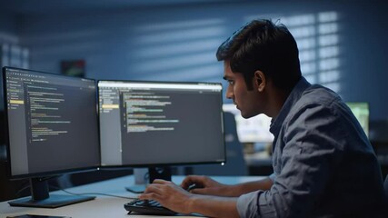 Man coding on computers at desk in office, focus on monitors