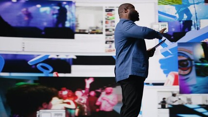 Poster - Black presenter hosting conference on stage surrounded by media visuals, symbolizing global convention with live audience to discuss about online trends and mobile apps. Public event. Camera A.