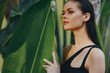 © SHOTPRIME STUDIO - Tropical Paradise Woman in Black Swimsuit Standing by Large Green Plant with Palm Tree in Background